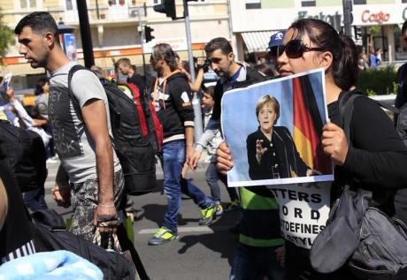 A womanl holds a picture of German Chancellor Angela Merkel as migrants set off on foot for the border with Austria from Budapest, Hungary, September 4, 2015. REUTERS/Bernadett Szabo